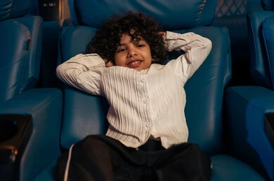 Expressions of relaxation and happiness, a Gulf Arab Saudi boy in the cinema hall, spending enjoyable times, recreational activities, watching movies and theatrical performances in the cinema, cinema and theater, background of the cinema screening room, exhibition hall.