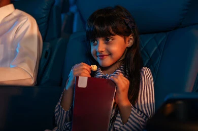 تعابير تدل على الإندماج، الإستمتاع بتناول الفشار، فتاة عربية خليجية سعودية في صالة السينما،قضاء أوقات ممتعة، أنشطة ترفيهية، مشاهدة الأفلام والعروض المسرحية في السينما، سينما ومسرح، خلفية قاعة عرض السينما، صالة العرض