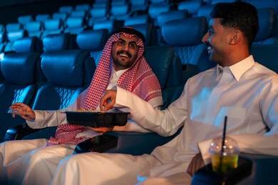 دور العرض الحديثة في المملكة العربية السعودية، الاستمتاع بتناول المقرمشات ذهبية اللون ، مشاهدة الأفلام والمسرحيات والعروض المتنوعة, شاشات ضوئية كبيرة لزيادة الاستمتاع بالتجربة، القيام بنشاطات ترفيهية ممتعة, رجلان عربيان خليجيان سعوديان يجلسان في قاعة السينما ويتابعان الفيلم بايماءات السعادة