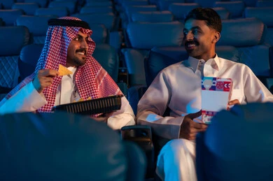 مشاهدة الأفلام والمسرحيات والعروض المتنوعة, شاشات ضوئية كبيرة لزيادة الاستمتاع بالتجربة، القيام بنشاطات ترفيهية ممتعة, رجلان عربيان خليجيان سعوديان يجلسان في قاعة السينما ويتابعان  الفيلم بايماءات السعادة, دور العرض الحديثة في المملكة العربية السعودية