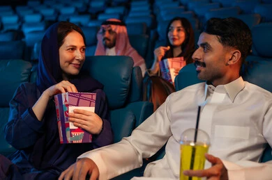 4D cinema halls, an Arab Saudi Gulf audience in the cinema hall, expressions indicating immersion, enjoying popcorn and cold drinks, recreational activities, spending enjoyable times, watching movies and theatrical performances in the cinema, cinema and theater, background of the cinema screening room.