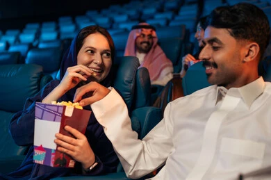 شاشات ضوئية كبيرة لزيادة الاستمتاع بالتجربة، القيام بنشاطات ترفيهية ممتعة, عائله عربية خليجية سعودية تجلس في قاعة السينما وتتابع الفيلم بتركيز, مشاهدة الأفلام والمسرحيات والعروض المتنوعة,  دور العرض الحديثة في المملكة العربية السعودية