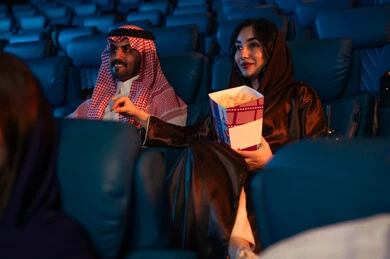 القيام بنشاطات ترفيهية ممتعة, قضاء أوقات سعيده، رجل عربي سعودي خليجي بجانب زوجته في صالة السينما، تعابير تدل على الإندماج، الإستمتاع بتناول الفشار والمشروبات الباردة ، مشاهدة الأفلام والعروض المسرحية في السينما، سينما ومسرح، خلفية قاعة عرض السينما، صالة العرض