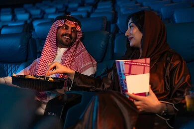 تعابير السرور والسعاده ، أنشطة ترفيهية سعيدة، قضاء أوقات ممتعة، رجل عربي سعودي خليجي بجانب زوجته في صالة السينما، تعابير تدل على الإندماج، الإستمتاع بتناول الفشار والمشروبات الباردة ، مشاهدة الأفلام والعروض المسرحية في السينما، سينما ومسرح، خلفية قاعة عرض السينما، صالة العرض