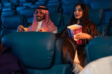 رجل عربي سعودي خليجي بجانب زوجته في صالة السينما، أنشطة ترفيهية سعيدة، قضاء أوقات ممتعة، تعابير تدل على الإندماج، الإستمتاع بتناول الفشار والمشروبات الباردة ، مشاهدة الأفلام والعروض المسرحية في السينما، سينما ومسرح، خلفية قاعة عرض السينما، صالة العرض