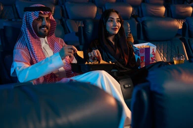 مفهوم المودة والالفه ، أنشطة ترفيهية سعيدة، قضاء أوقات ممتعة، رجل عربي سعودي خليجي بجانب زوجته في صالة السينما، تعابير تدل على الإندماج، الإستمتاع بتناول الفشار والمشروبات الباردة ، مشاهدة الأفلام والعروض المسرحية في السينما، سينما ومسرح، خلفية قاعة عرض السينما، صالة العرض