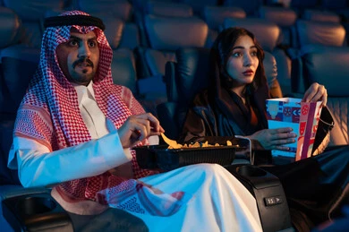 Enjoying popcorn, happy recreational activities, spending enjoyable times, an Arab Saudi Gulf man next to his wife in the cinema hall, expressions indicating engagement, watching movies and theatrical performances in the cinema, cinema and theater, background of the cinema screening room, exhibition hall. Enjoying popcorn, happy recreational activities, spending enjoyable times, an Arab Saudi Gulf man next to his wife in the cinema hall, expressions indicating engagement, watching movies and theatrical performances in the cinema, cinema and theater, background of the cinema screening room, exhibition hall.