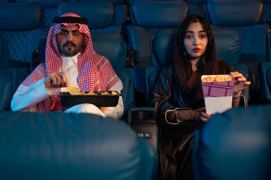 مشاهدة الأفلام والعروض المسرحية في السينما، أنشطة ترفيهية سعيدة، قضاء أوقات ممتعة، رجل عربي سعودي خليجي بجانب زوجته في صالة السينما، تعابير تدل على الإندماج، الإستمتاع بتناول الفشار والمشروبات الباردة ،سينما ومسرح، خلفية قاعة عرض السينما، صالة العرض