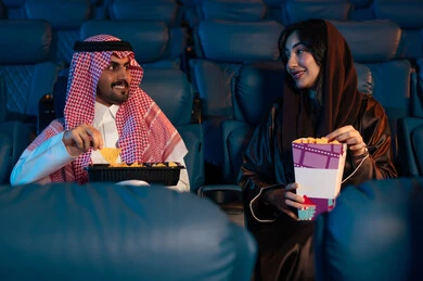 أنشطة ترفيهية سعيدة، قضاء أوقات ممتعة، رجل عربي سعودي خليجي بجانب زوجته في صالة السينما، تعابير تدل على الإندماج، الإستمتاع بتناول الفشار والمشروبات الباردة ، مشاهدة الأفلام والعروض المسرحية في السينما، سينما ومسرح، خلفية قاعة عرض السينما، صالة العرض