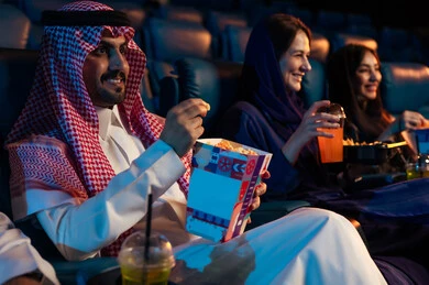 أنشطة ترفيهية سعيدة، قضاء أوقات ممتعة، جمهور عربي سعودي خليجي في صالة السينما، تعابير تدل على الإندماج، الإستمتاع بتناول الفشار والمشروبات الباردة ، مشاهدة الأفلام والعروض المسرحية في السينما، سينما ومسرح، خلفية قاعة عرض السينما، صالة العرض