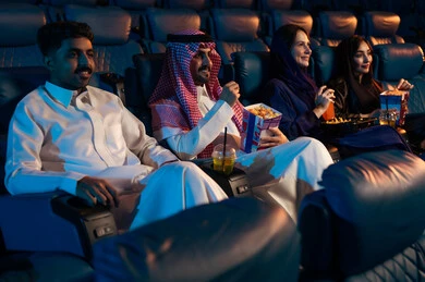 Expressions indicating integration, enjoying popcorn and cold drinks, an Arab Saudi Gulf audience in the cinema hall, recreational activities, spending enjoyable times, watching movies and theatrical performances in the cinema, cinema and theater, background of the cinema screening room, exhibition hall.