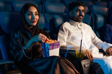 Modern cinemas in the Kingdom of Saudi Arabia, happy recreational activities, spending enjoyable times, an Arab Saudi Gulf man in the cinema hall with his wife, enjoying popcorn and cold drinks, watching movies and theatrical performances in the cinema, cinema and theater, background of the cinema screening hall, exhibition hall.