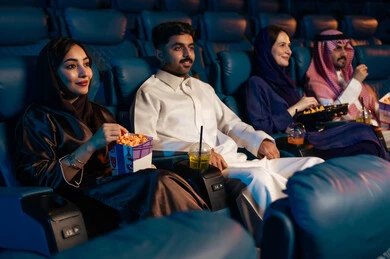 Distinctive recreational activities, expressions indicating integration, enjoying popcorn and cold drinks, an Arab Saudi Gulf audience in the cinema hall, spending enjoyable times, watching movies and theatrical performances in the cinema, cinema and theater, background of the cinema screening room, exhibition hall.