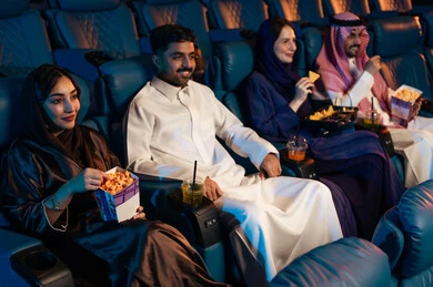 Spending enjoyable times, watching movies and theatrical performances in the cinema, expressions indicating engagement, enjoying popcorn and cold drinks, an Arab Saudi Gulf audience in the cinema hall, recreational activities, cinema and theater, background of the cinema screening room, the screening hall.