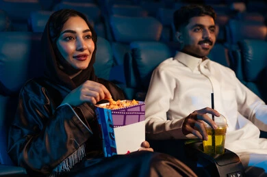 A Saudi Arabian Gulf man in a cinema hall with his wife, happy recreational activities, spending enjoyable times, enjoying popcorn and cold drinks, watching movies and theatrical performances in the cinema, cinema and theater, background of the cinema screening room, exhibition hall. A Saudi Arabian Gulf man in a cinema hall with his wife, happy recreational activities, spending enjoyable times, enjoying popcorn and cold drinks, watching movies and theatrical performances in the cinema, cinema and theater, background of the cinema screening room, exhibition hall.