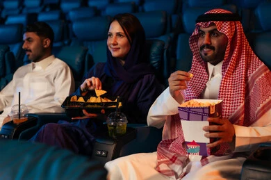 Expressions indicating integration, enjoying popcorn and cold drinks, an Arab Saudi Gulf audience in the cinema hall, recreational activities, spending enjoyable times, watching movies and theatrical performances in the cinema, cinema and theater, background of the cinema screening room, exhibition hall.