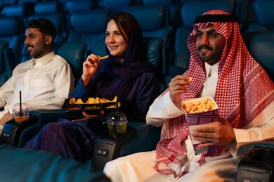 الإستمتاع بتناول الفشار والمقرمشات ذهية اللون ،تعابير تدل على الإندماج، جمهور عربي سعودي خليجي في صالة السينما، أنشطة ترفيهية، قضاء أوقات ممتعة، مشاهدة الأفلام والعروض المسرحية في السينما، سينما ومسرح، خلفية قاعة عرض السينما، صالة العرض