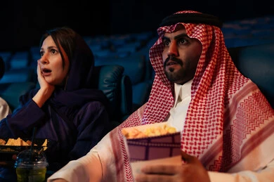 مشاهدة الأفلام المرعبه والعروض المسرحية في السينما، تعابير الخوف والذعر ،الاثارة والتشويق والاندماج ، قضاء أوقات ممتعة، رجل عربي سعودي خليجي في صالة السينما برفقة زوجته، الإستمتاع بتناول الفشار والمشروبات الباردة ، سينما ومسرح، خلفية قاعة عرض السينما، صالة العرض