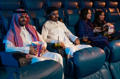 Large screens to enhance the enjoyment of the experience, engaging in fun recreational activities, an Arab Gulf Saudi audience sitting in the cinema hall watching the film with gestures of happiness, watching movies, plays, and various shows, modern theaters in the Kingdom of Saudi Arabia.