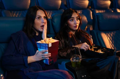 Watching horror movies and theatrical performances in the cinema, expressions of fear and terror, excitement and suspense and immersion, spending enjoyable times, two Arab Saudi Gulf friends in the cinema hall, enjoying popcorn and cold drinks, cinema and theater, background of the cinema screening room, the exhibition hall.