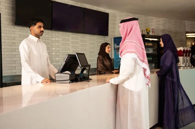 أنشطه ترفيهيه متميزة ، مشاهدة الأفلام والعروض المسرحية ، رجل عربي سعودي خليجي يرتدي الزي التقليدي والشماغ يقوم بحجز تذكرة   لمشاهدة فيلم في صالة السينما