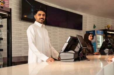 مشاهدة الأفلام والعروض المسرحية ، موظف عربي سعودي خليجي مبتسم يرتدي الزي التقليدي ينظر الى الكاميرا فى صاله حجز التذاكر لمشاهدة فيلم في صالة السينما، أنشطه ترفيهيه متميزة