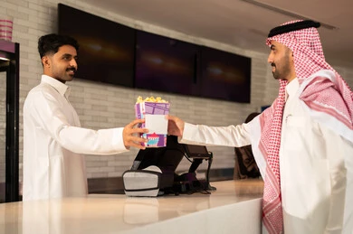 أنشطه ترفيهيه متميزة، رجل عربي سعودي خليجي مبتسم يرتدي الزي التقليدي والشماغ يقوم بشراء الفشار فى صاله حجز التذاكر لمشاهدة فيلم في صالة السينما، متابعة الأفلام والعروض المسرحية