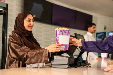 أنشطه ترفيهيه متميزة، سيدة عربية سعودية خليجية مبتسمة ترتدي العباءة والحجاب تقوم بشراء الفشار فى صاله حجز التذاكر لمشاهدة فيلم في صالة السينما، متابعة الأفلام والعروض المسرحية