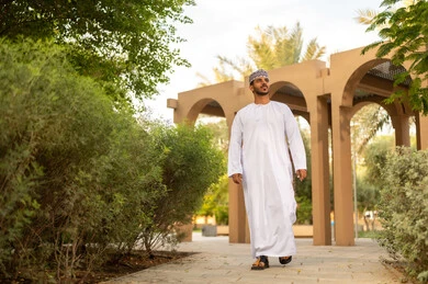 قضاء عطله نهاية الاسبوع فى الخارج، الاستمتاع بالهواء الطلق والزهور، المنتزهات والحدائق العامة، رجل عربي خليجي عماني يرتدي الدشداشة و الكمة يقوم بالمشي فى احد الحدائق و ينظر الى الاعلي
