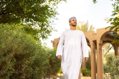 المنتزهات والحدائق العامة، قضاء أوقات ممتعة فى الهواء الطلق، رجل عربي خليجي عماني يرتدي الدشداشة و الكمة يقوم بالمشي فى احد الحدائق و ينظر الى الاعلي ، الاستمتاع بالهواء الطلق والزهور