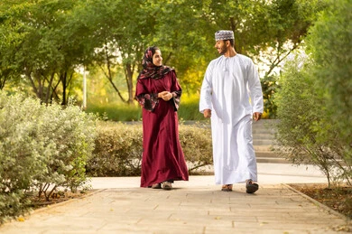 التآلف والود بين أفراد العائلة، مفهوم العلاقات الزوجية الناجحة السعيده، قضاء عطلة نهاية الاسبوع في أحد الحدائق ،زوجان عربيان خليجيان عمانيان يرتديان الزي التقليدي يقومان بتبادل الأحاديث والدردشات