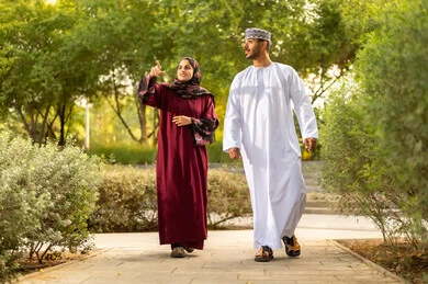 مفهوم العلاقات الزوجية الناجحة السعيده، الاشارة الى شيء ما، قضاء عطلة نهاية الاسبوع في أحد الحدائق ،زوجان عربيان خليجيان عمانيان يرتديان الزي التقليدي يقومان بتبادل الأحاديث والدردشات