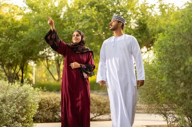 الاشارة الى شيء ما،  مفهوم العلاقات الزوجية الناجحة السعيده، قضاء عطلة نهاية الاسبوع في أحد الحدائق ،زوجان عربيان خليجيان عمانيان يرتديان الزي التقليدي يقومان بتبادل الأحاديث والدردشات