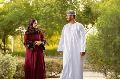 أوقات مليئة بالود والمشاعر الطيبة، مفهوم العلاقات الزوجية الناجحة السعيده، قضاء عطلة نهاية الاسبوع في أحد الحدائق ،زوجان عربيان خليجيان عمانيان يرتديان الزي التقليدي يقومان بتبادل الأحاديث والدردشات
