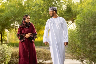 جو مليء بالمحبة والتقارب العائلي، مفهوم العلاقات الزوجية الناجحة السعيده، قضاء عطلة نهاية الاسبوع في أحد الحدائق ،زوجان عربيان خليجيان عمانيان يرتديان الزي التقليدي يقومان بتبادل الأحاديث والدردشات