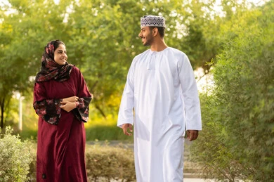 التنزه في الهواء الطلق، اجواء مليئة بالمحبة والود، مفهوم العلاقات الزوجية الناجحة السعيده، قضاء عطلة نهاية الاسبوع في أحد الحدائق ،زوجان عربيان خليجيان عمانيان يرتديان الزي التقليدي يقومان بتبادل الأحاديث والدردشات