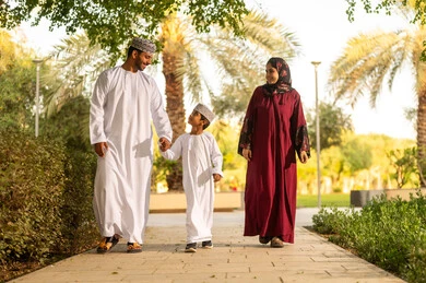 لحظات عائلية مليئة بالمرح, أنشطة ترفيهية عائلية في العطلة، عائله عربية خليجيه عمانية ترتدي الزي التقليدي تقوم بالمشي فى احدي الحدائق برفقة ابنهم بايماءات السعادة و السرور ، قضاء اوقات ممتعه مع الابناء