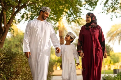 أجواء أسرية ممتعة, أنشطة ترفيهية عائلية في العطلة، عائله عربية خليجيه عمانية ترتدي الزي التقليدي تقوم بالمشي فى احدي الحدائق برفقة ابنهم بايماءات السعادة و السرور ، قضاء اوقات ممتعه مع الابناء
