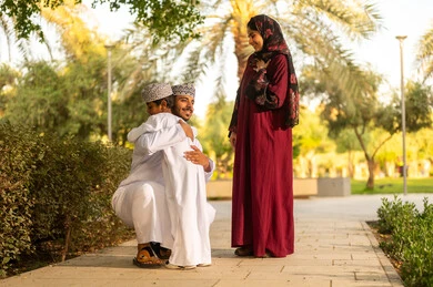The concept of family bonding, spending the weekend holiday abroad, an Omani Gulf Arab family dressed in traditional attire enjoying a pleasant time in one of the parks, an Omani father wearing the dishdasha and kumma embracing his son.