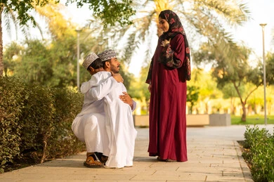 Spending the weekend holiday abroad, the concept of family bonding, an Omani Gulf Arab family wearing traditional attire enjoying a pleasant time in one of the parks, an Omani father wearing a dishdasha and kumma embracing his son.