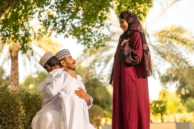 عائله عربيه خليجيه عمانية ترتدي الزي التقليدي تقوم بالاستمتاع بقضاء ممتع فى احدي الحدائق ، اب عماني يرتدي الدشداشة و الكمه يقوم باحتضان ابنه ، مفهوم الترابط الاسري ، قضاء عطله نهايه الاسبوع فى الخارج