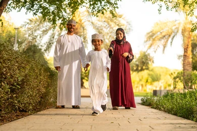 حديقة ومنتزه عائلي ترفيهي، عائلة عربية خليجية عمانية يرتدون الزي التقليدي يمشون في إحدى الحدائق العامة في النهار، الإستمتاع باللعب في يوم مشمس، تقوية وتعزيز الروابط الأسرية، الاستمتاع بالنزهة في الهواء الطلق, قضاء الوقت الممتع مع الأسرة