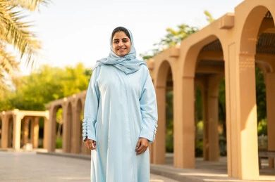 Looking at the camera with gestures of happiness and joy, a young Saudi woman stands upright and with self-esteem, caring about her appearance. An Arab Gulf woman from Oman wearing a hijab and an abaya is taking a stroll outdoors in one of the parks and recreational areas.