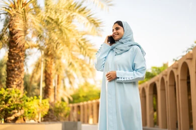 دمج التكنولوجيا والتقنيات الحديثة في الحياة اليومية، إمرأة عمانية ترتدي العباءة والحجاب تقوم باجراء مكالمه هاتفية عبر الجوال، ايماءات وتعابير السعادة و السرور، شابة عربية خليجية سعودية تستخدم الهاتف المحمول، استخدام جهاز تقني حديث، القيام بنزهه في الهواء الطلق في احدى الحدائق والمنتزهات