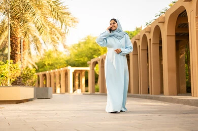 القيام بجولة ترفيهية في الحديقة،  قضاء أوقات ممتعة، إمرأة عمانية ترتدي العباءة والحجاب تقوم باجراء مكالمه هاتفية عبر الجوال، ايماءات وتعابير السعادة و السرور، شابة عربية خليجية سعودية تستخدم الهاتف المحمول، استخدام جهاز تقني حديث