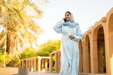 إمرأة عمانية ترتدي العباءة والحجاب تقوم باجراء مكالمه هاتفية عبر الجوال، ايماءات وتعابير السعادة و السرور، شابة عربية خليجية سعودية تستخدم الهاتف المحمول تتجول في إحدى الحدائق العامة، استخدام جهاز تقني حديث، قضاء أوقات ممتعة،  القيام بنزهه في الهواء الطلق في احدى الحدائق والمنتزهات