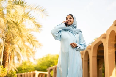 ايماءات وتعابير السعادة و السرور، شابة عربية خليجية سعودية تستخدم الهاتف المحمول تتجول في إحدى الحدائق العامة، استخدام جهاز تقني حديث، قضاء أوقات ممتعة، إمرأة عمانية ترتدي العباءة والحجاب تقوم باجراء مكالمه هاتفية عبر الجوال،  القيام بنزهه في الهواء الطلق في احدى الحدائق والمنتزهات