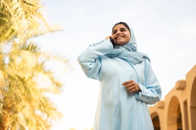 استخدام جهاز تقني حديث، شابة عربية خليجية سعودية تستخدم الهاتف المحمول تتجول في إحدى الحدائق العامة، قضاء أوقات ممتعة، ايماءات وتعابير السعادة و السرور، إمرأة عمانية ترتدي العباءة والحجاب تقوم باجراء مكالمه هاتفية عبر الجوال،  القيام بنزهه في الهواء الطلق في احدى الحدائق والمنتزهات