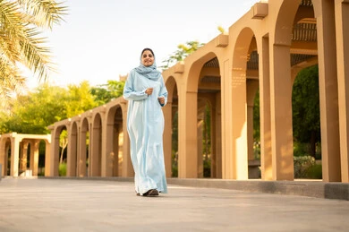 Taking a walk outdoors and relaxing, a Saudi Arabian Gulf woman practicing walking, enjoying natural parks, a young Omani woman in a hijab wearing an abaya taking a stroll in the garden, wandering and walking in green parks.