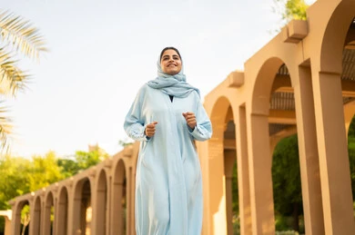 A Saudi Arabian Gulf woman practices walking, going for a stroll outdoors and relaxing, enjoying natural parks. A young Omani woman in a hijab wearing an abaya is taking a walk in the park, wandering and walking in green gardens.